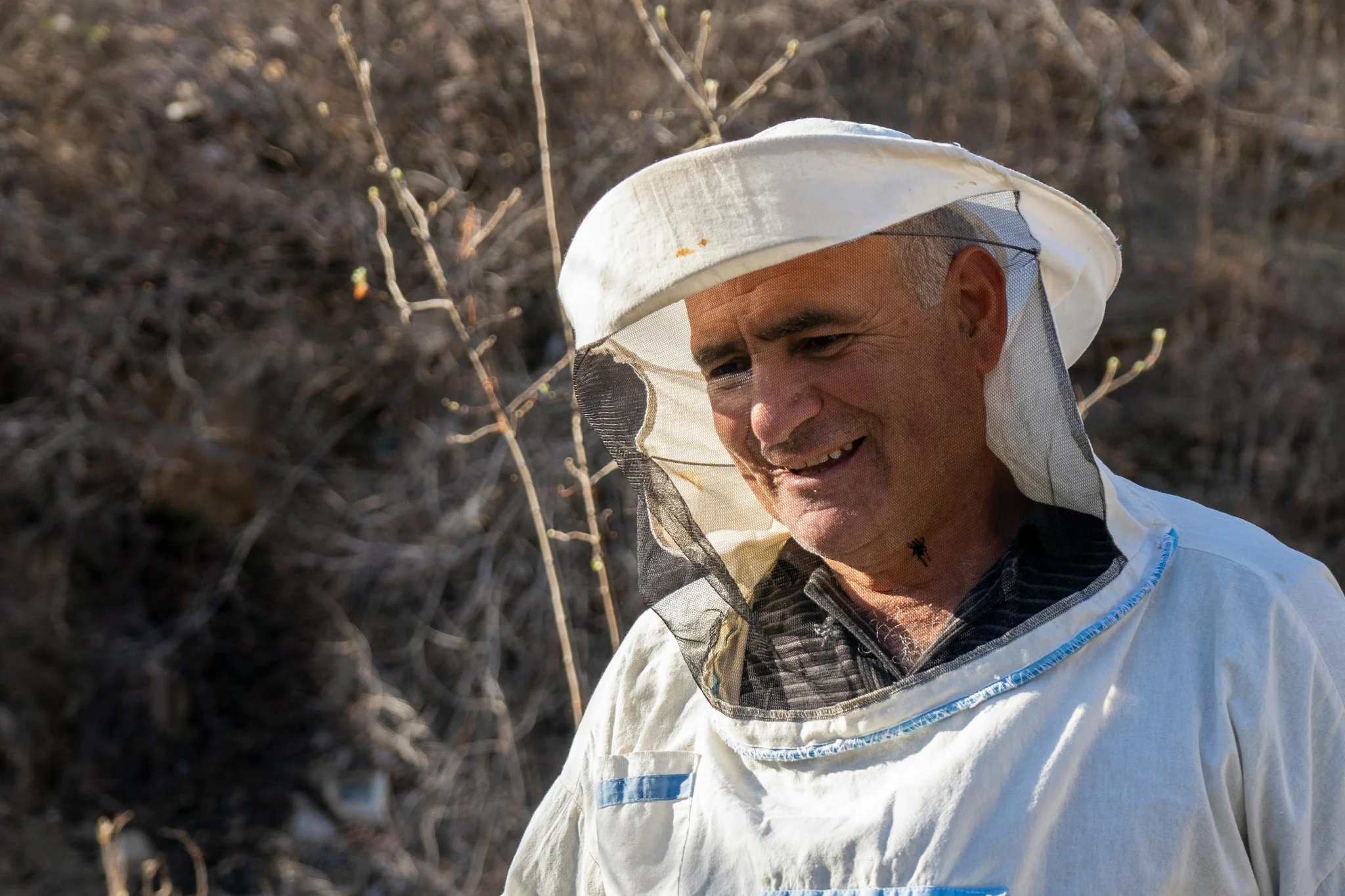 Portrait d’un apiculteur souriant devant ses ruches en pleine nature